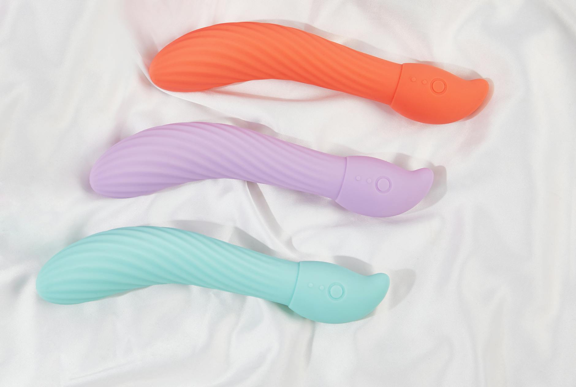 A hand reaching over a variety of colorful sex toys arranged on a table, showing exploration and choice.