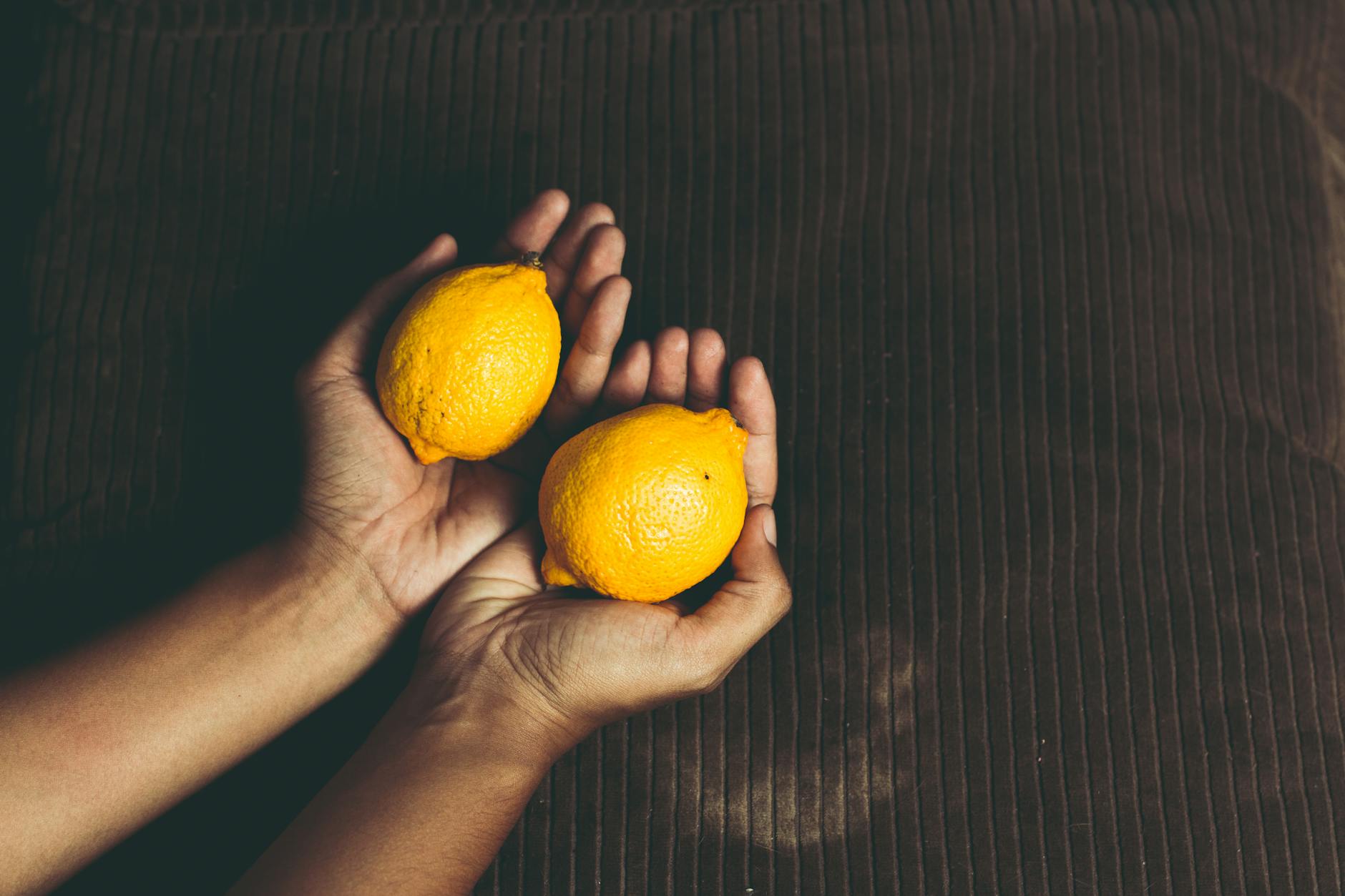 Manos sosteniendo limones frescos sobre una superficie marrón, simbolizando la frescura y el cuidado natural