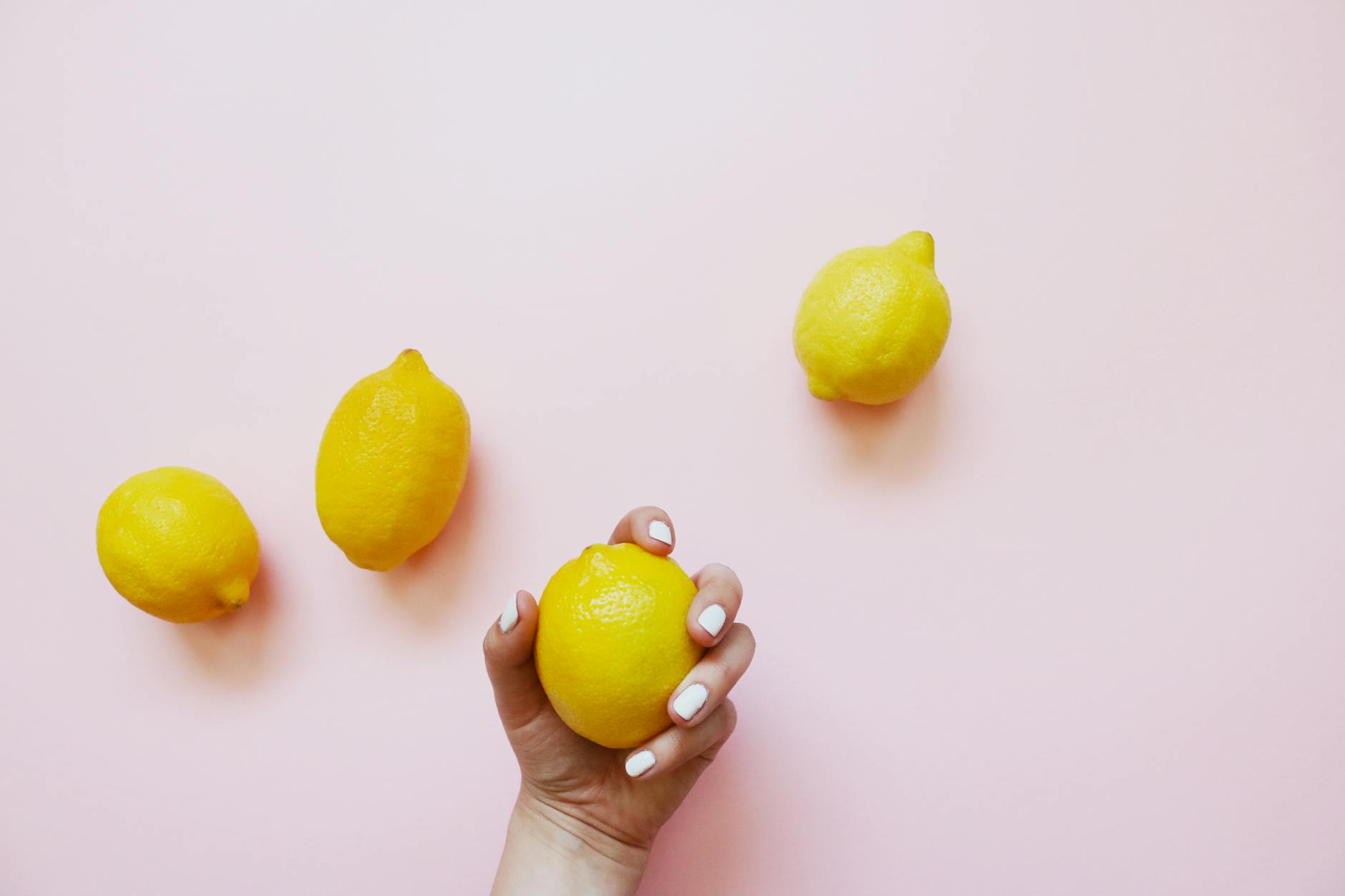 Una mano sosteniendo un limón fresco sobre un fondo rosa suave, simbolizando la sensibilidad y el cuidado al tocar