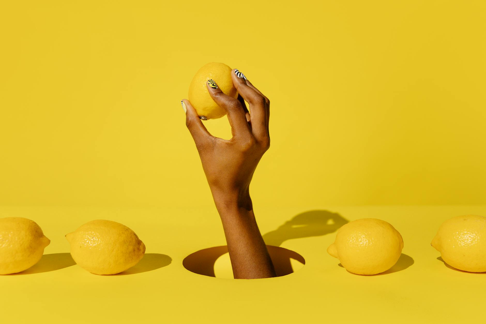 A hand holding a fresh lemon against a bright yellow background, symbolizing the direct, efficient approach of clitoral stimulation