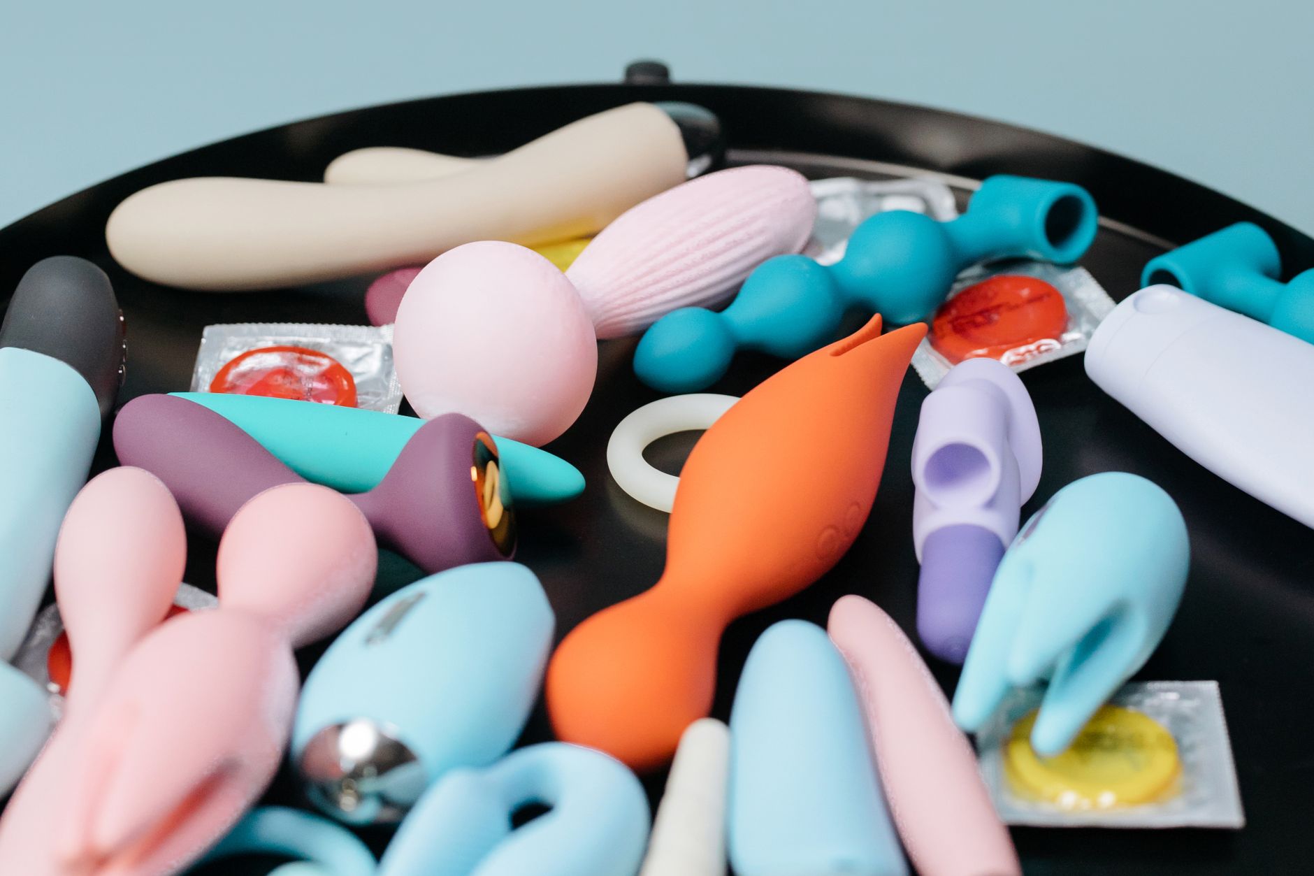A vibrant collection of various clitoral vibrators on a black tray, featuring diverse shapes and colors