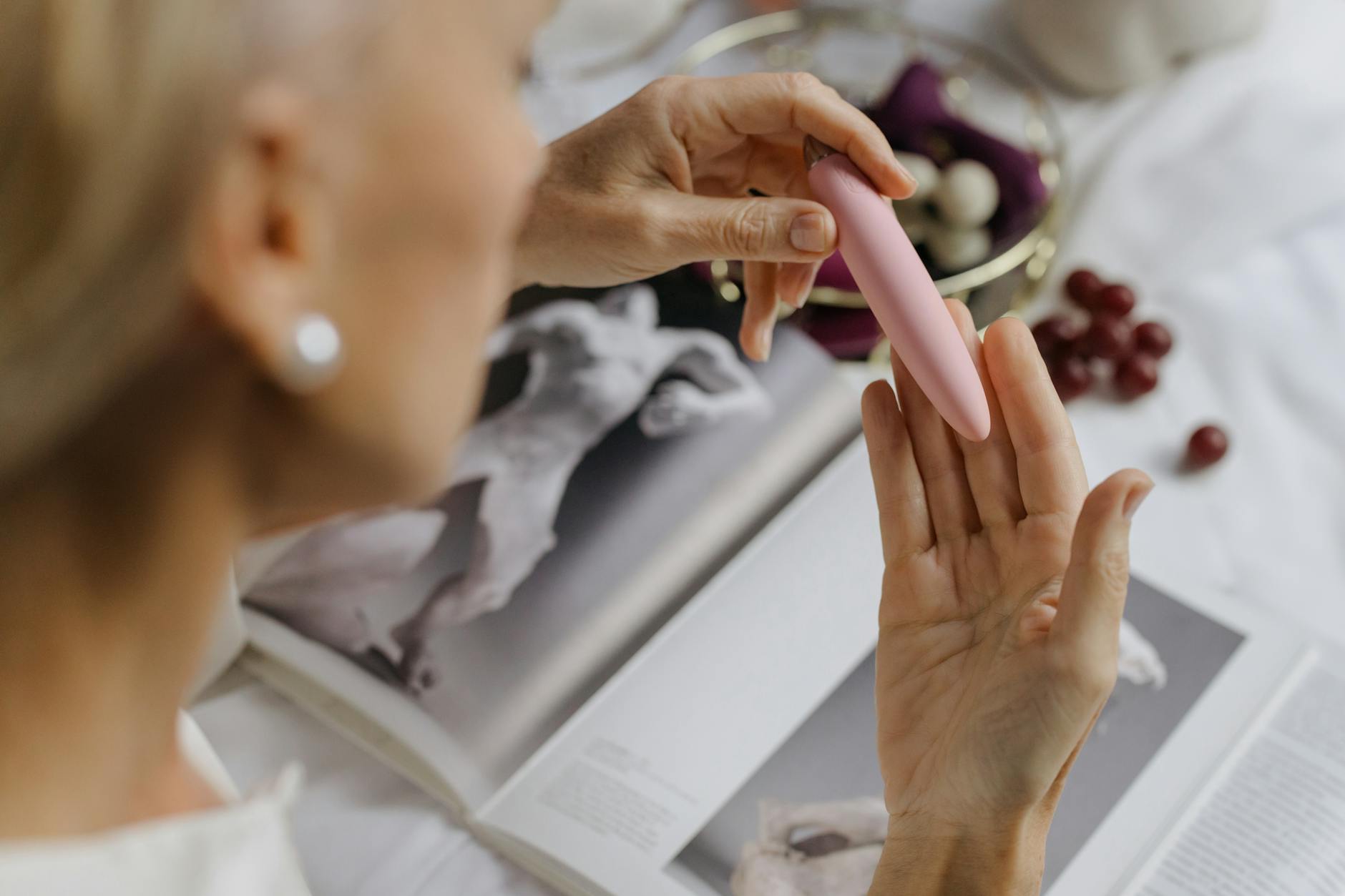 Primer plano de una mujer sosteniendo un vibrador rosa con libros de arte de fondo, enfatizando temas íntimos y personales.