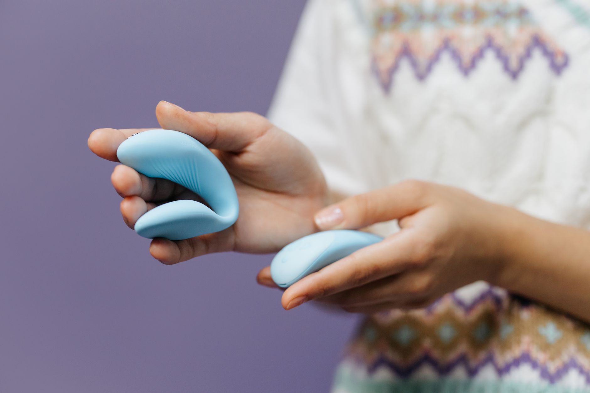 Close-up of hands holding a sleek blue vibrator against a purple background, symbolizing solo pleasure and personal healing.