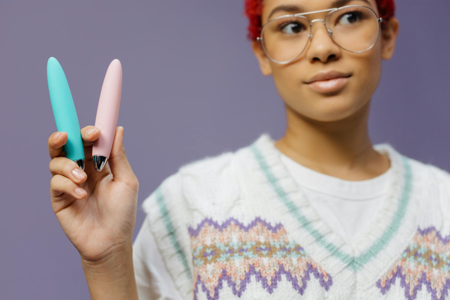 Woman holding colorful vibrators against a purple background, representing sexual wellness and intimacy tools.