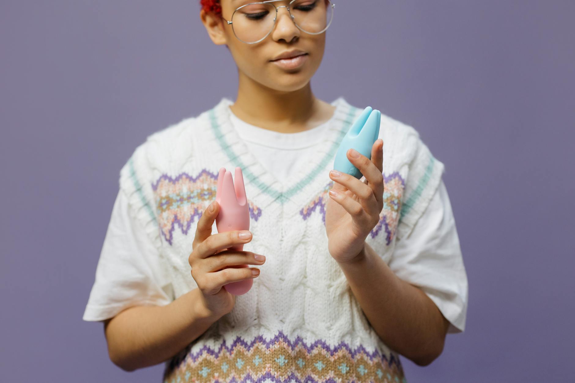 Mujer joven sosteniendo vibrador clitoridiano rosa y azul contra fondo púrpura